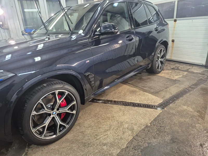 Ciemne BMW w hali Detail-Wash, zbliżenie na bok i przednie koło