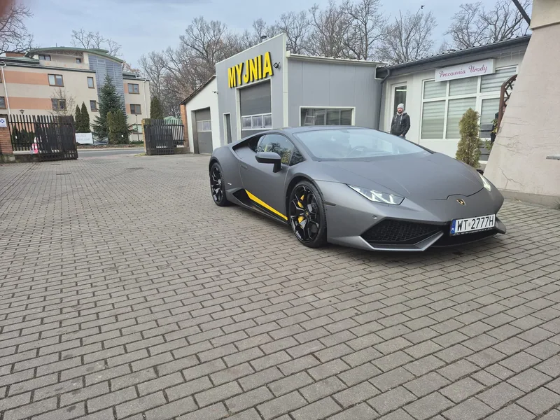 Szare Lamborghini przy żółtym szyldzie MYJNIA